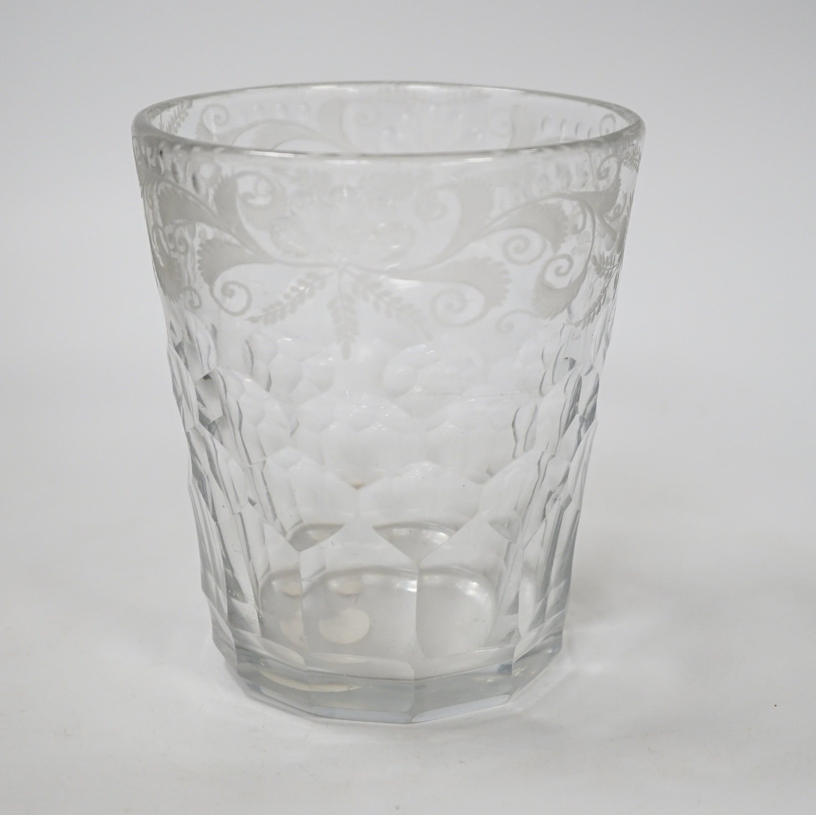 An English lead crystal 18th century faceted tumbler, in a darkish grey metal, upper decoration engraved and polished floral centre, three rows of facets running into plain facets, whole of foot polished to remove pontil